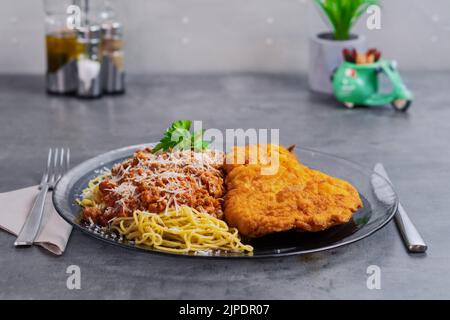Spaghetti milanesi con costolette fritte su un tavolo grigio Foto Stock