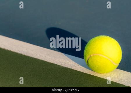 Palla da tennis gialla sulla linea di base su un nuovo campo da tennis blu con verde fuori limite. Foto Stock