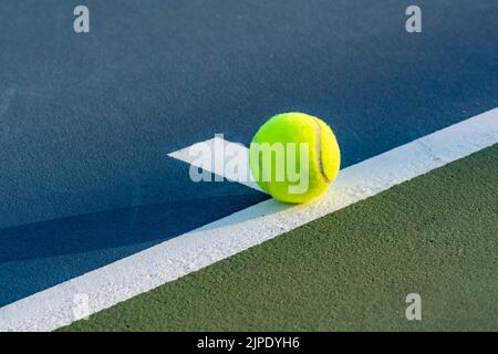 Palla da tennis gialla sulla linea di base al punto centrale su un nuovo campo da tennis blu con verde fuori limite. Foto Stock