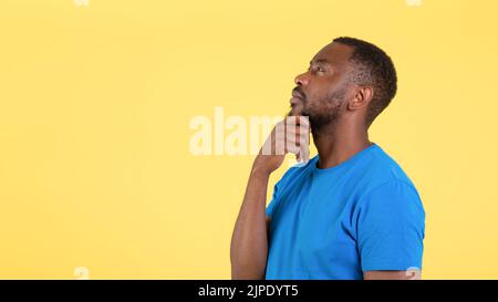 Vista laterale dell'uomo nero che pensa in piedi su sfondo giallo Foto Stock