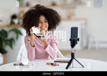 Ragazza pre-teen nera che fa trucco e registrazione vlog sul telefono Foto Stock