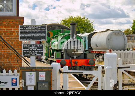 Treno a vapore alla piattaforma visto attraverso le indicazioni nella stazione ferroviaria di Lincolnshire Wolds Railway, Ludborough, Inghilterra, Regno Unito Foto Stock