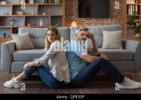 Infelice maschio caucasico maturo con barba ignora donna offesa, sedersi sul pavimento di nuovo a schiena Foto Stock