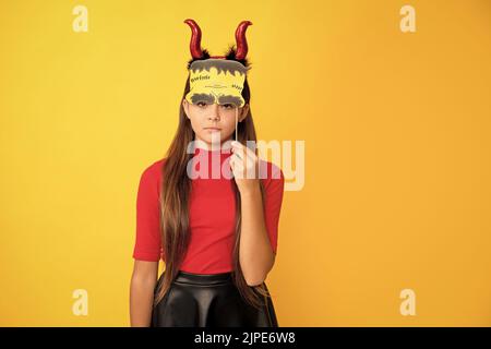 ragazza teen seria che indossa corna imp che tiene accessorio del partito su sfondo giallo, halloween Foto Stock