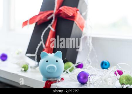 Sotto l'albero di Natale sono scatole con i regali. Sulla scatola c'è una piccola banca di porcellini. Bella carta festiva. Foto Stock