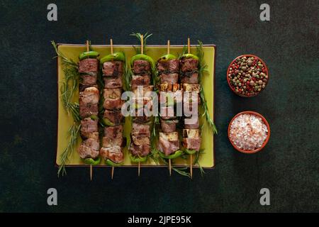 Spiedini di carne al forno su un piatto verde con sale e pepe misto. Foto Stock