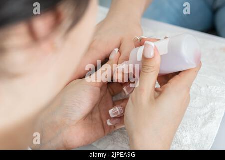 dettaglio delle mani di una ragazza manicurista, effettuando una pulizia, applicando con la bottiglietta un liquido per pulire la cuticola delle unghie. donna Foto Stock