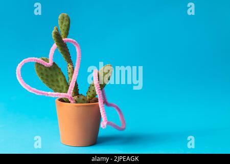 Cuori rosa sulle foglie di cactus, mini cactus in vaso di terra isolato su sfondo blu. Nessuna gente, nessuno. Spazio di copia, spazio per il testo. Foto Stock