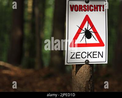 Gallner, Baviera, Germania, 15 agosto 2022, Cartello di avvertimento su un albero in una foresta buia con iscrizione tedesca di attenzione, zecche Foto Stock