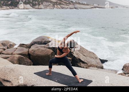 Donna sana praticando Utthita Parsvakonasana yoga posa. Donna che si esercita vicino ad un oceano. Foto Stock