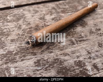 Particolare di una marijuana illuminata o di un'articolazione di erbacce raffigurata su un tavolo di legno marrone all'aperto. Foto Stock