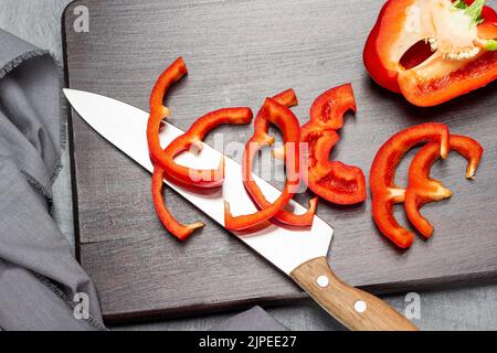 Coltello da cucina, pepe rosso tritato e mezzo pepe sul tagliere. Giacitura piatta. Sfondo grigio. Foto Stock