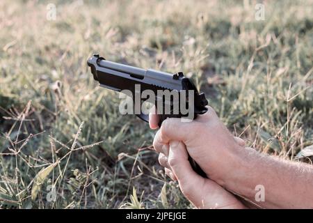 pistola con le mani maschili, le dita tirano il grilletto. Maneggiando armi, sparando per strada. Foto Stock