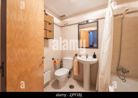 Bagno piastrellato in marmo con lavandino a piedistallo in porcellana bianca abbinato, specchio con cornice in metallo e vasca da bagno ricurvata Foto Stock