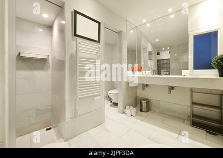 Grande bagno piastrellato con marmo bianco, piano di appoggio con due lavandini, grande specchio che copre una parete e cabine separate per doccia e wc Foto Stock