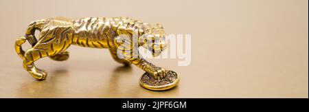 Banner con una figura di bronzo di una tigre con una moneta - il simbolo del benessere finanziario e della ricchezza su uno sfondo dorato, Copy Space. Foto Stock