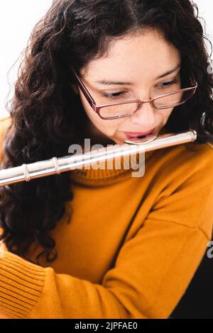 Primo piano di una donna bruna che indossa un maglione giallo e che gioca un flauto trasversale. Verticale Foto Stock