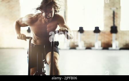 Fa tutto a 100. Un giovane bell'uomo che guarda pieno di determinazione mentre si lavora su un addestratore ellittico. Foto Stock