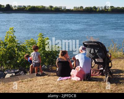 Una famiglia giovane con due bambini che fa un picnic sulla riva del fiume Foto Stock