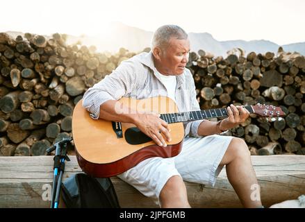. Uomo maturo, rilassandosi e suonando la chitarra mentre si siede all'aperto e si gode il suo hobby mentre si respira aria fresca. L'uomo più anziano canta una canzone nel suo Foto Stock