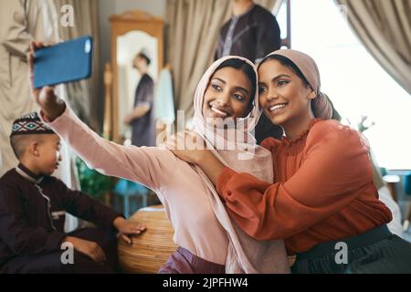 Sorelle musulmane che prendono selfie in sciarpa islamica tradizionale della testa all'interno di una casa felice della famiglia insieme. Belle giovani donne che ne sono orgogliose Foto Stock