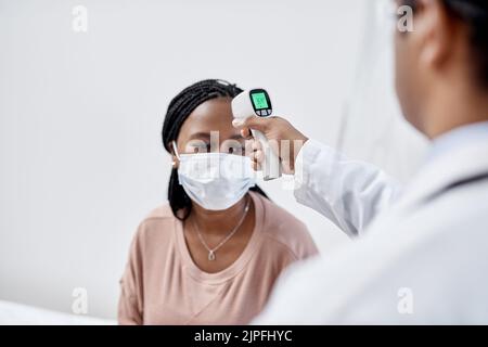 Medico che prende la temperatura di un paziente covid mentre prova per i sintomi di febbre alta di malattia, influenza o malattia. Donna di screening per una consulenza sanitaria Foto Stock