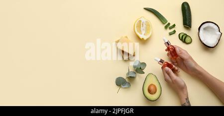 Mani femminili con bottiglie di olio essenziale e ingredienti naturali su sfondo beige con spazio per il testo Foto Stock