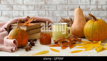 Composizione autunnale con libri, tazza di tè aromatico, barattolo di gustosa marmellata e cracknell a tavola Foto Stock