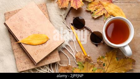 Composizione autunnale con libri, tazza di tè aromatico e occhiali da sole su sfondo ligneo Foto Stock