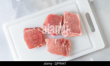 Braciole di maiale crudo in primo piano sul tagliere, giacitura piatta, fondo in marmo Foto Stock