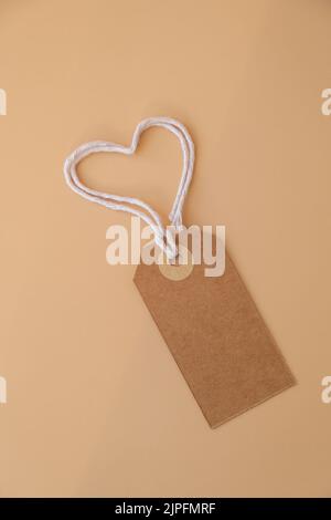 Nota in carta beige monocromatica e corda a forma di cuore su sfondo beige neutro. Biglietto di auguri vacanza idea. Simponi spazio di copia per il testo. Regalo Foto Stock