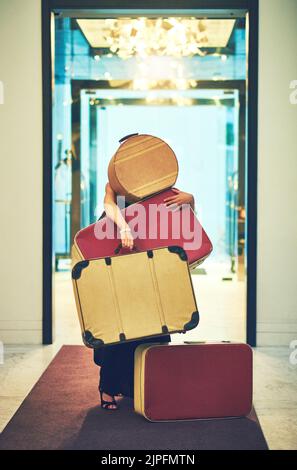 Sono io che viaggio con leggerezza, una giovane donna irriconoscibile che porta con sé un sacco di bagagli mentre cerco di scendere nell'atrio di un hotel. Foto Stock