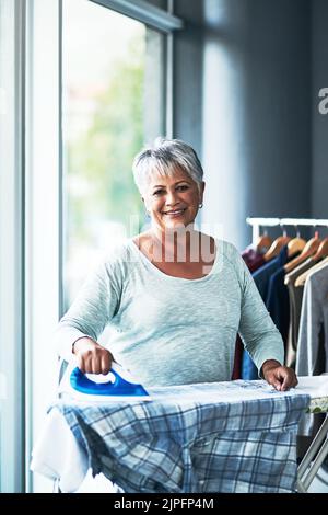 Le pieghe non sono uguali per me. Ritratto di una donna matura che stira abiti a casa. Foto Stock