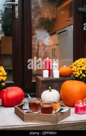 Vassoio di legno con tè speziato con arancia sul portico della casa decorata con zucche, fiori e candele. Accogliente ingresso casa decorata per trad Foto Stock