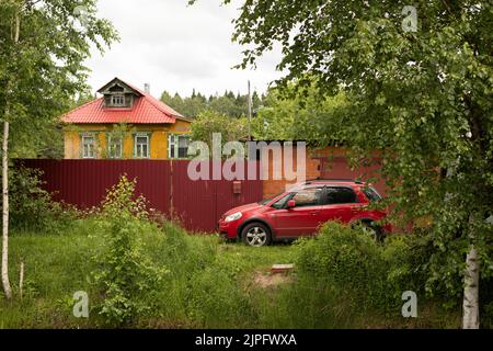 Auto vicino casa in campagna. Parcheggio in casa privata. Macchina rossa. Trasporto per famiglie. Foto Stock