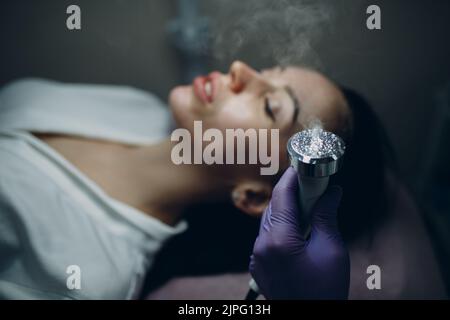 Primo piano della donna di testa che riceve l'elettroporazione phonoforesis terapia facciale presso il salone di bellezza Foto Stock