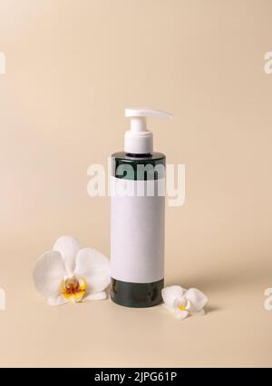 Bottiglia cosmetica scura con un'etichetta vuota vicino a fiori di orchidea bianca su giallo chiaro, vista dall'alto, mockup. Prodotti di bellezza fatti a mano per la cura della pelle, tonico o. Foto Stock