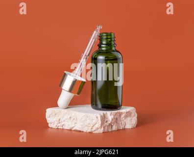 Flacone contagocce verde aperto su pietra beige su primo piano rosso, Mockup cosmetico. Prodotti di bellezza per la cura della pelle, siero o olio essenziale. Cosmetici naturali Foto Stock