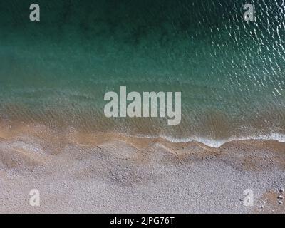 Vista aerea dall'alto sul mare azzurro e sulla spiaggia di ciottoli rosa. Piccole onde sulla superficie dell'acqua cristallina in movimento. Estate mare spiaggia Foto Stock