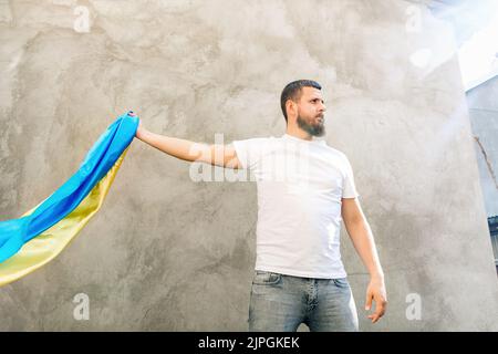 L'uomo tiene in mano la bandiera blu e gialla dell'Ucraina. Ragazzo in T-shirt e jeans bianchi. Giorno di sole. Costituzione e Indipendenza giorno dell'Ucraina. Vista inferiore della foto. Messa a fuoco selettiva morbida Foto Stock