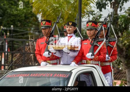 Bangli, Bali, Indonesia. 17th ago, 2022. Il portatore di bandiera della cerimonia, affiancato da membri dell'esercito indonesiano, porta la bandiera nazionale rossa e bianca del paese. 1,130 studenti delle scuole superiori della reggenza di Bangli hanno creato una folla di carta raffigurante la bandiera nazionale indonesiana, il rosso e il bianco, e le parole ''buon 77th° anniversario, Repubblica di Indonesia'' per commemorare la giornata dell'indipendenza della nazione, che si celebra il 17 agosto di ogni anno. L'Indonesia ha dichiarato l'indipendenza il 17 agosto 1945. (Credit Image: © Dicky Bisinglasi/ZUMA Press Wire) Foto Stock