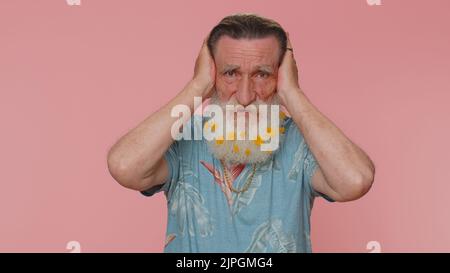 Non vuoi ascoltare e ascoltare. Frustrato irritato anziano irritato coprendo le orecchie e gesturando no, evitando consiglio ignorando rumore sgradevole voce forte. Nonno sullo sfondo rosa delle pareti dello studio Foto Stock