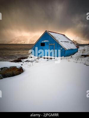 Blue Boat House durante un tramonto Blizzard, Godøy, Sunnmøre, Møre og Romsdal, Norvegia. Foto Stock