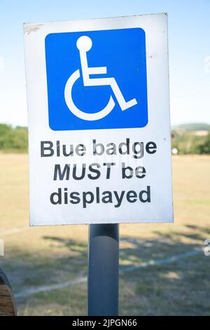 Primo piano del cartello presso il parcheggio per disabili presso il campo sportivo del Regno Unito, in cui viene indicato ai titolari di badge blu che i permessi per disabili blu devono essere esposti nei veicoli. Foto Stock