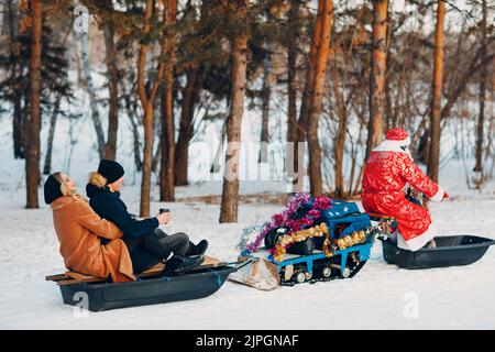 Babbo natale in sella a una coppia di motoslitte innamorata nella foresta invernale. Foto Stock