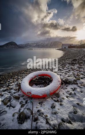 Lifebuoy su una spiaggia di ciottoli durante il tramonto invernale a Godøy, Sunnmøre, Møre og Romsdal, Norvegia. Foto Stock