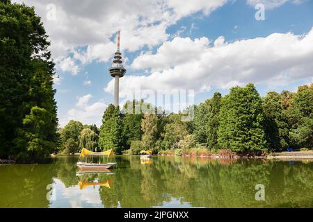 La Telecommunications Tower nel parco Luisenpark di Mannheim, in Germania, con un laghetto e lussureggianti alberi verdi sullo sfondo Foto Stock