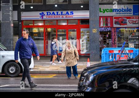 LONDRA - 20 maggio 2022: Persone che attraversano la trafficata strada di Londra tra i taxi Foto Stock