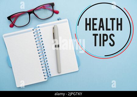 Una scrittura che mostra il testo 'consigli per la salute' con blocco note e occhiali su sfondo blu Foto Stock