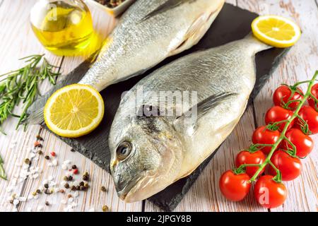 Pesce fresco dorado e ingredienti per la cottura. Pesce crudo dorada con spezie ed erbe su tavola grigia in cemento. Frutti di mare, ristorante, dieta, cibo sano b Foto Stock